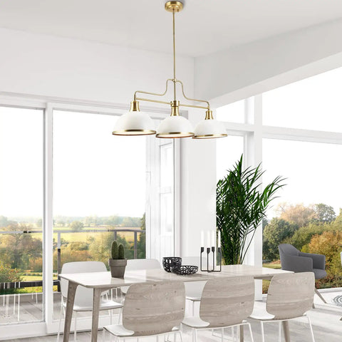 Three Light Linear Chandelier In Matte White With Brass Accents hanging over modern dining table in bright room.