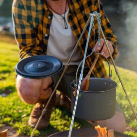 Person with Ultralight Aluminum Hanging Camping Pot With Lid, 4.2 Quart Cookware For 4 To 6 People over campfire
