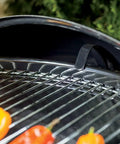 Close-up of Original Kettle Charcoal Grill 22-Inch Black With One-Touch Cleaning System showing steel grate with peppers
