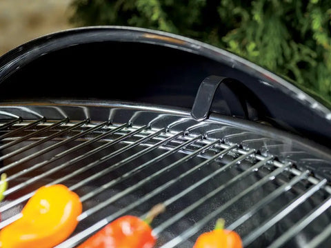 Close-up of Original Kettle Charcoal Grill 22-Inch Black With One-Touch Cleaning System showing steel grate with peppers