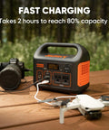 Portable Power Station Explorer 300 293Wh Backup Battery Solar Generator next to camera and drone on wooden table outdoors