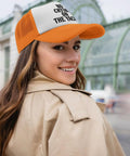 Woman wearing Breathable Men's Trucker Hat For Running And Everyday Wear With No Sweat Band, orange, outdoors.