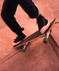 Person skateboarding down a concrete ramp at sunset, wearing black shoes and jeans, showcasing balance and movement.