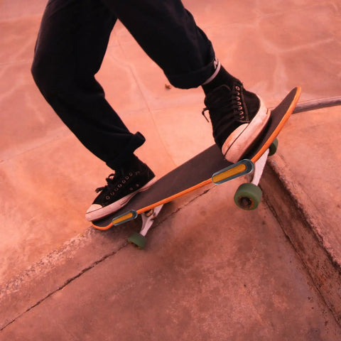 Person skateboarding down a concrete ramp at sunset, wearing black shoes and jeans, showcasing balance and movement.