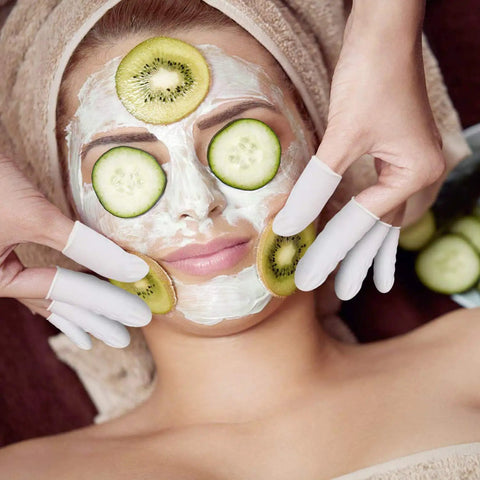 Two hands wearing large 4 mil thick disposable latex finger cots apply cucumber slices in spa facial.