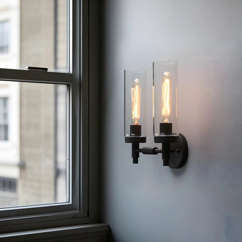 Rustic Industrial Wall Sconce Light With Tubular Clear Glass Lampshades, Matte Black Finish, mounted by a window, lit
