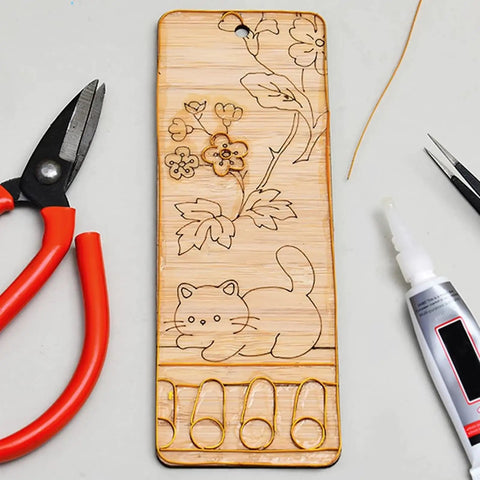 Wooden board with floral and cat engravings, red-handled pliers, and glue, featuring Dual Color Cloisonne Wire Set 20m Gold and Silver 0.3mm Thick Wire With 1mm Diameter Jewelry Making Tools Kit Includes Two Wire Straightening Boards for DIY Metalwork Home Decor Gift Crafting for Beginners and Pros