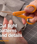 Premium No.5 Micro-Tip Fabric Scissors with orange handle cutting fabric, ideal for intricate patterns. Premier No 5 Micro Tip Orange Handled Fabric Scissors With Double Loop Handle For Precise Sewing Crafting And Detail Cutting Of Intricate Patterns For Tiny Details And Tight Patterns On Fine Fabrics And Delicate Projects.