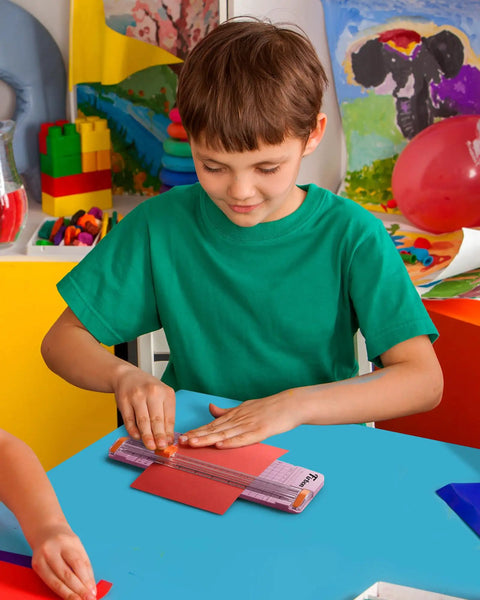 Child using Pink A5 Paper Cutter Guillotine with Side Ruler for Scrapbooking in a colorful classroom setting.
