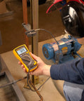 Technician using Pro Grade HVAC Multimeter And Clamp Meter Kit to measure AC DC voltage near a motor in industrial setting.