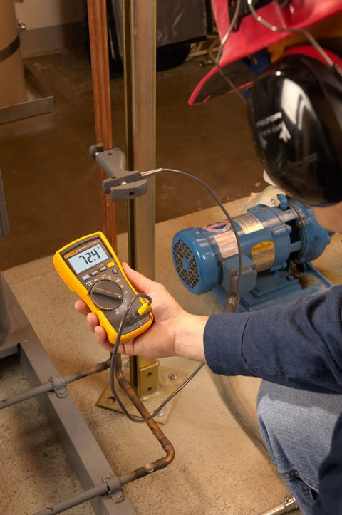 Technician using Pro Grade HVAC Multimeter And Clamp Meter Kit to measure AC DC voltage near a motor in industrial setting.