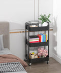 3 Tier Plastic Rolling Utility Cart With Handle For Office Kitchen And Living Room next to a bed, multifunctional storage trolley with books and decor items.