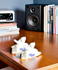 Two white Audiowipes towelettes crumpled on a wooden desk beside a stack of books and a speaker.