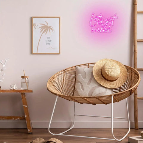 Lets Get Naked Pink Neon Sign For Bedroom Decor LED Neon Light Wall Art in a cozy room with chair, wall art, and ladder, 15.7x11.8 inches.
