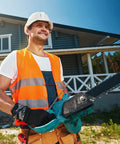 Construction worker holding a chainsaw in front of a modern house, wearing safety gear.