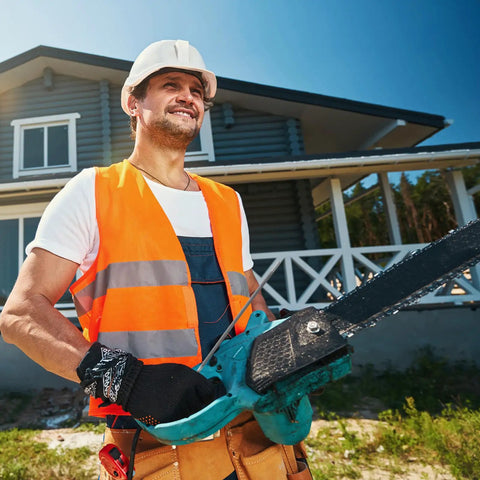 Construction worker holding a chainsaw in front of a modern house, wearing safety gear.