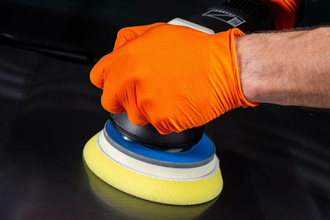 Close-up of orange nitrile glove with diamond-textured grip on a polishing machine with blue and yellow foam pad