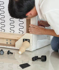 Man installing 20 Pack Black Adjustable Furniture Leveling Pads Anti Slip Shims under a sofa to reduce vibration