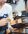 Man applying Dope Shoe Glue For Sole Repair Quick Dry Waterproof Adhesive Clear 60ml 45g to worn shoe sole in workshop.