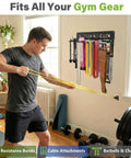 Person using resistance bands next to 8 Hook Wall Mount Home Gym Organizer Rack For Barbells Resistance Bands Jump Ropes Foam Rollers Belts And More Garage Grade Heavy Duty Gear Storage Solution With All Hardware Included.