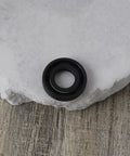 Close-up of black nitrile rubber oil seal with double lip, 12x24x4.5 mm, on stone surface