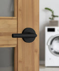 Interior Passage Door Lever For Closet And Hallway Doors No Lock Reversible Handle Matte Black Finish Easy Install Durable Dual Spring Design Keeps Lever Upright And Wobble Free For Smooth Everyday Use on wooden door with washing machine in background