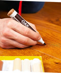 Close-up of 6 Piece Wood Furniture Repair Markers Set for concealing scratches on wood surfaces, hand using oak pen.
