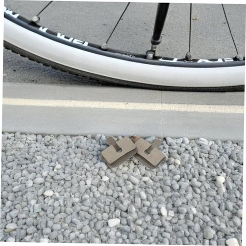 2 Pairs Bike Disc Brake Pads For Hydraulic And Mechanical Disc Brakes Replacement Pads next to bicycle tire on gravel