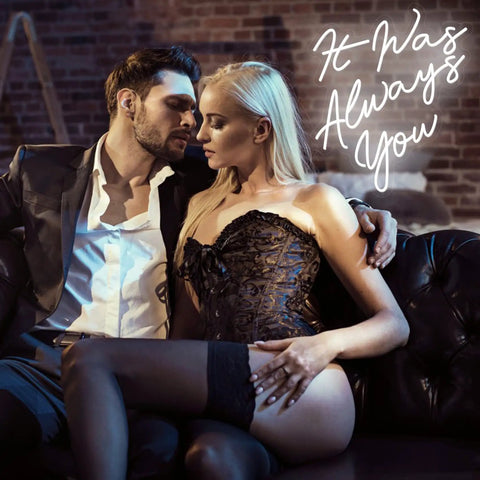 Couple embracing on sofa with 'It Was Always You' neon sign glowing in background, creating a romantic atmosphere.