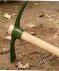 Steel Garden Pickaxe With Wooden Handle For Weeding And Soil Cultivation, Durable Hand Hoe resting on soil with green blade.