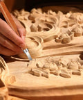 Close-up of hands using a chisel on detailed floral wood carving