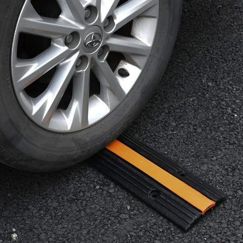 Heavy Duty Rubber Cable Ramp 2 Channel Drive Over Protector under car wheel on asphalt, showing durability and use.