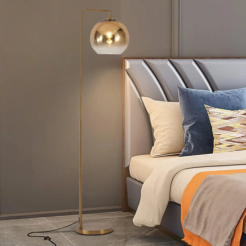 Gradient Gold Floor Lamp With Glass Globe LED Standing Light In Modern Mid Century Style next to bed in bedroom.