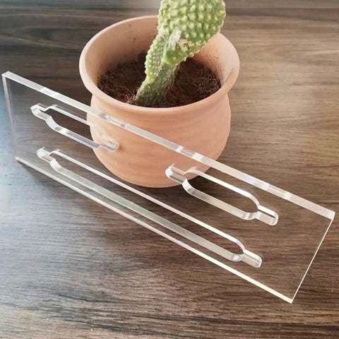 Slick Clear Acrylic Keyhole Slot Routing Template For Hanging Picture Frames And Woodworking Projects Features One Quarter Inch Thick Hardened Material With Dust Vents For Router Bits Plus Three Sizes For No Fuss Do It Yourself Installations next to a potted cactus.