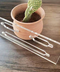 Game Changer Clear Acrylic Keyhole Slot Template Router Jig For Picture Hanging And Woodworking Shop Projects Pre Cut Slots on wood surface with a plant.