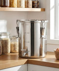 Straight Up Heavy Duty 304 Stainless Steel Beverage Dispenser With Easy Flow Spigot on kitchen counter next to jars of grains.