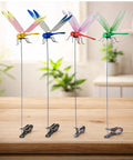 Multicolor 12-Pack dragonfly clips on table, showing colorful designs on metal stakes for garden decor; Dope Dragonfly Clip 12 Pack For Garden Decor And Outdoor Stakes DIY Fake Dragonfly Clips For Hair Accessories, Pets, Patio Enhancement, And Plant Stems Multicolor 3D Dragonfly Charms