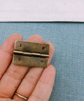 Hand holding a mini antique bronze hinge from the Forty Two Piece Antique Bronze Mini Iron Hinges Set With Rounded Corners