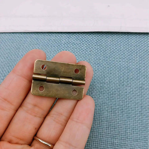 Hand holding a mini antique bronze hinge from the Forty Two Piece Antique Bronze Mini Iron Hinges Set With Rounded Corners