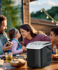 NEWBULIG countertop ice maker with handle, portable black ice machine on an outdoor table.