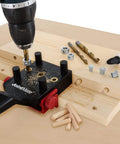 Self Centering Dowel Jig Kit For Woodworking in use with handheld jig, metal bushings, drill, dowels, and wood pieces for joints.