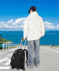 Boy with Three Piece Boys Rolling Backpack Set For School And Travel With Six Wheel Trolley Design on road overlooking ocean