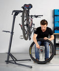 Heavy Duty Bike Repair Stand With 85 Lb Capacity holding mountain bike, mechanic adjusting wheel, adjustable height, foldable design