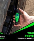 Rhino USA digital tire pressure gauge, black with green LCD display, held to a car tire valve during tire check.