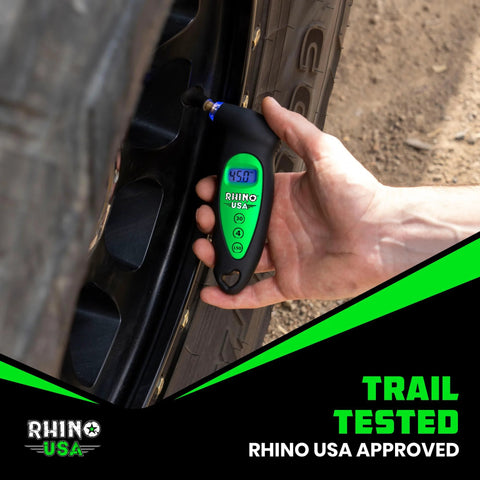 Rhino USA digital tire pressure gauge, black with green LCD display, held to a car tire valve during tire check.