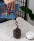Keep Your Beans Fresh As A Daisy With This Smart Electric Vacuum Seal Coffee Canister And Airtight Storage Jar For Whole Ground Roasts Real Deal Smooth Push Button Operation Durable Borosilicate Glass, hand pouring beans into glass canister.