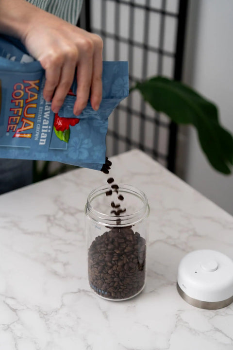 Keep Your Beans Fresh As A Daisy With This Smart Electric Vacuum Seal Coffee Canister And Airtight Storage Jar For Whole Ground Roasts Real Deal Smooth Push Button Operation Durable Borosilicate Glass, hand pouring beans into glass canister.