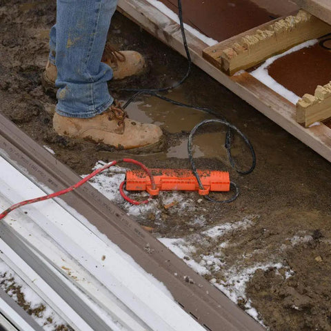 Heavy Duty Outdoor Extension Cord Safety Cover and Weatherproof Connector Protector in mud and snow, bright orange, 10-16 gauge cords