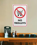 No Trolley Symbol 8 By 12 Warehouse Equipment Restriction Sign in indoor setting above a shelf with bottles and cups.