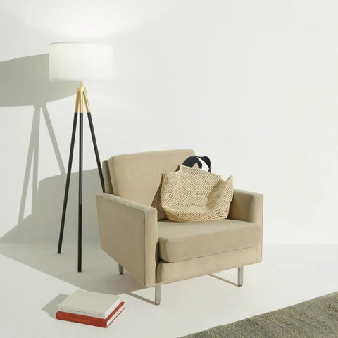 Levi LED Floor Lamp With Tall Black And Gold Tripod For A Dope Living Room Vibe next to beige armchair and books